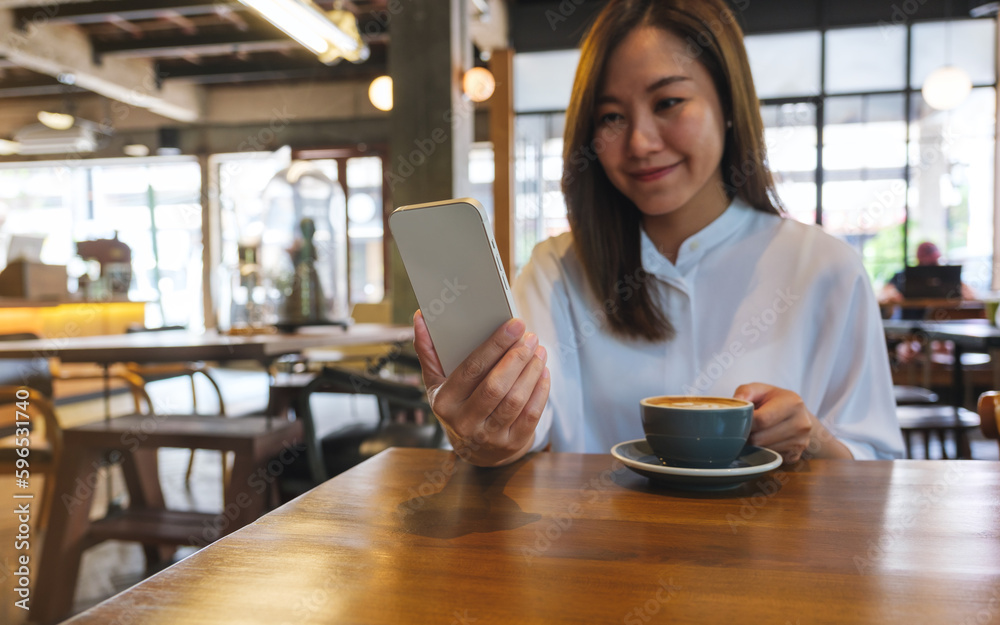 Portrait image of a young woman holding and using mobile phone while drinking coffee in cafe