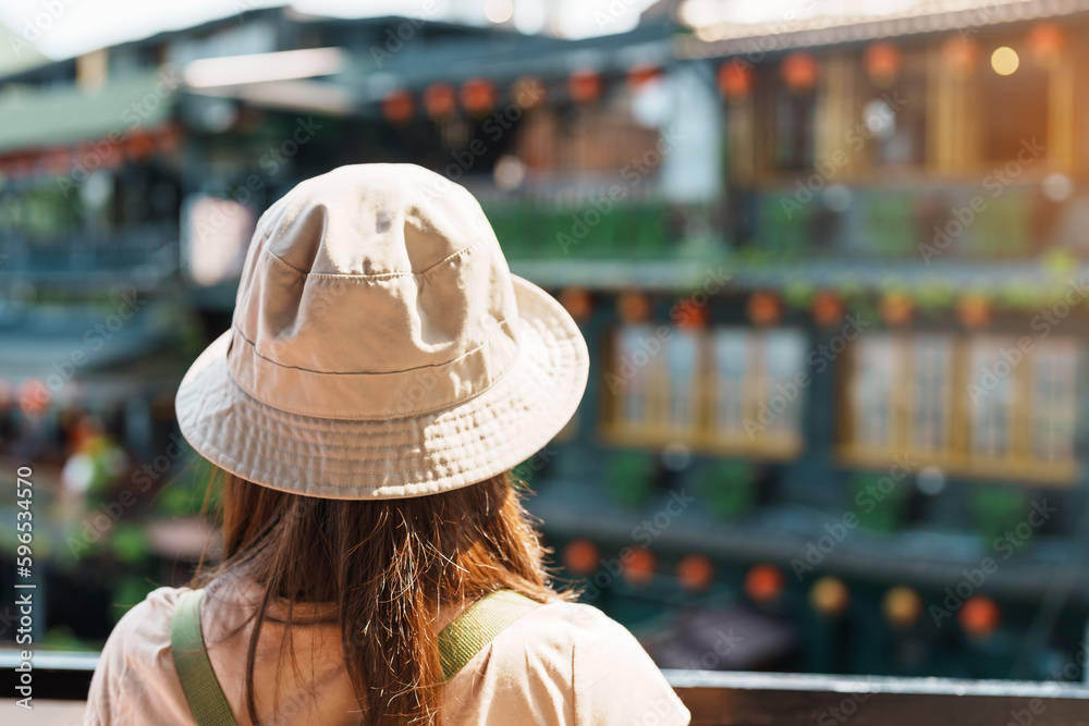 woman traveler visiting in Taiwan, Tourist with hat and backpack sightseeing in Jiufen Old Street village with Tea House background. landmark and popular attractions near Taipei city. Travel concept