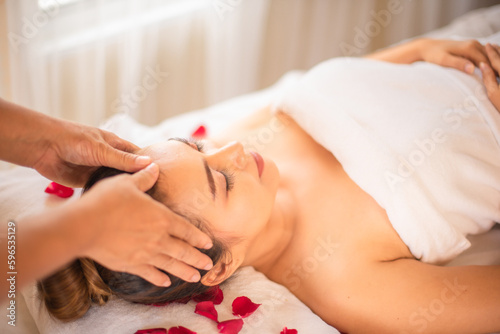 As the massage continues the client on bed sprinkled with rose petals in spa room feels more and more at ease her worries and stresses melting away.