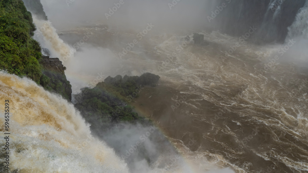 A powerful stream of water collapsing into a raging river. A rainbow in ...