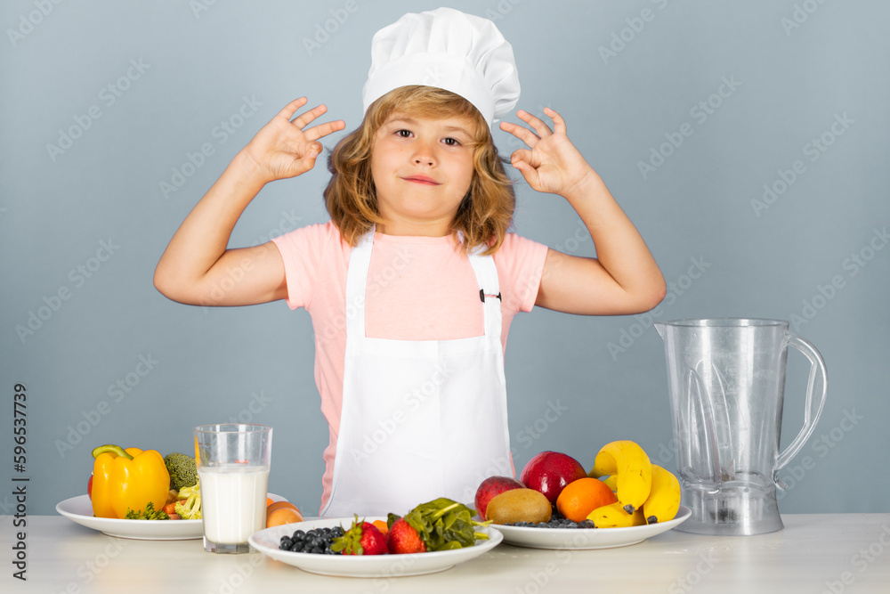 Fruits and vegetables for kids. Child chef cook prepares food on isolated grey studio background. Kids cooking. Teen boy with apron and chef hat preparing a healthy vegetables meal in the kitchen. Fruits and vegetables for kids. Child chef cook prepares food on isolated grey studio background. Kids cooking. Teen boy with apron and chef hat preparing a healthy vegetables meal in the kitchen.