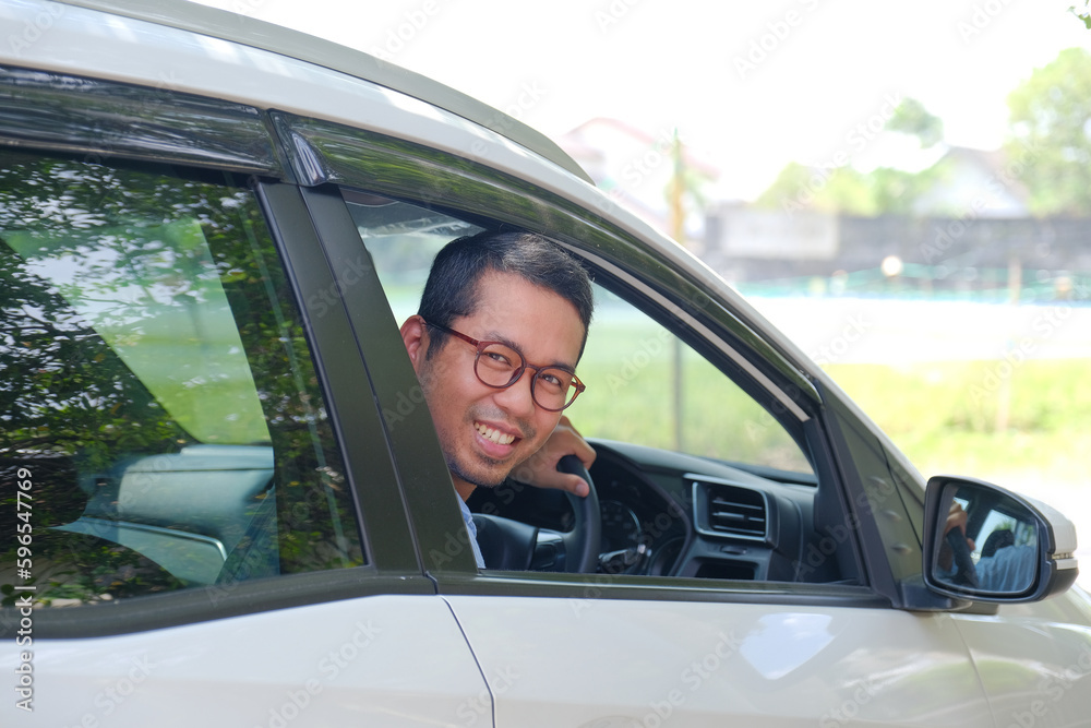Asian man looking behind from inside his car with happy expression