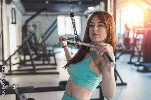 Sporty red-hair woman doing hard exercise at the gym