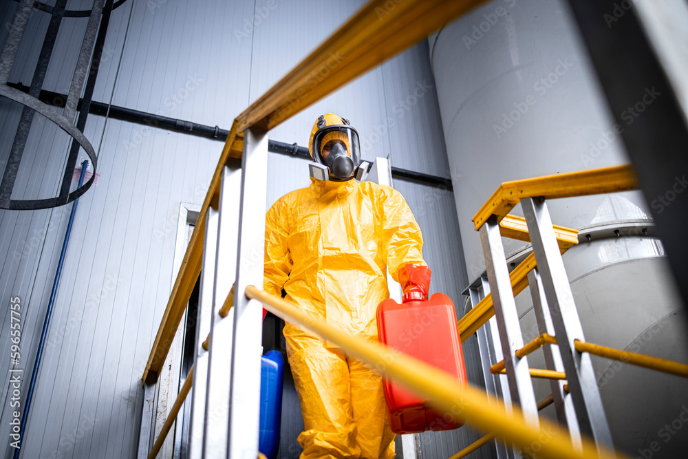 Factory worker wearing protective suit and gas mask carrying chemicals through industrial production plant.