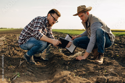 Two farmers are taking a sample of soil from the field to check it's fertility. photo