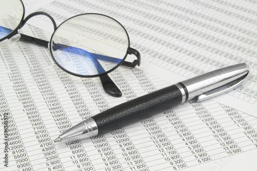 Black eyeglasses and pen on financial documents with many numbers. Statistics and accountancy concept.