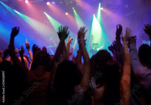 Fans  people or dancing at concert  music festival or night party  neon lights or event energy. Dance  fun and show  excited crowd in arena and rock band musician in spotlight on stage performance.