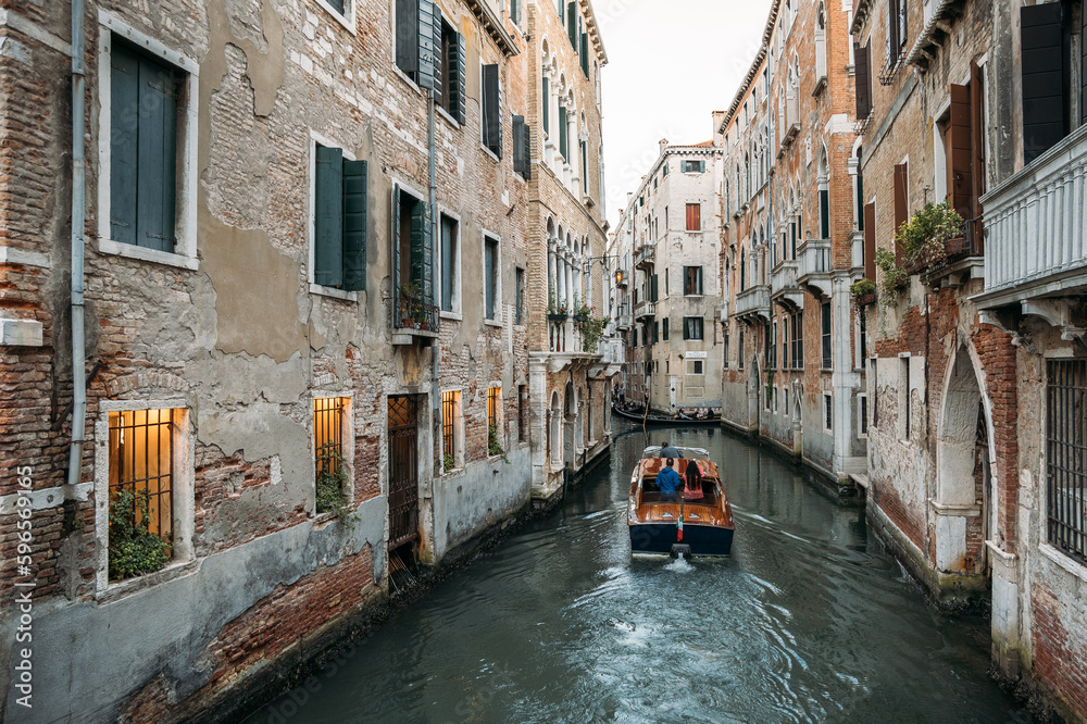 A boat sailing through the narrow canals of Venice between ancient stone houses. The concept of a unique European city in Italy