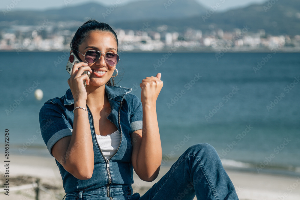 young latin hispanic woman with phone and success gesture with sea background