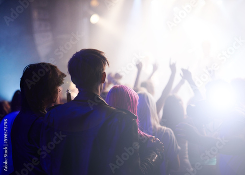 Dance, rock and friends in crowd at music festival from back, watching live band performance on stage. Audience in arena, lights and group of people at party, fans of musician at concert together.