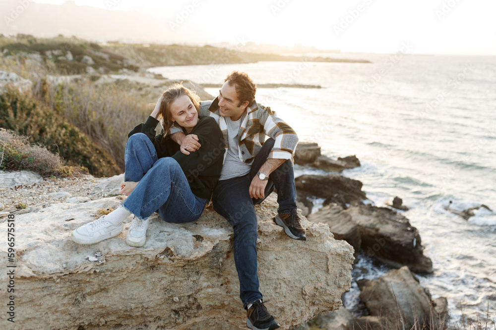 Portrait of a middle-aged couple sitting on a rock at the beach in Cyprus. They are wearing casual clothes. Relationships concept.
