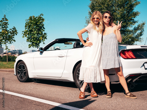 Two young beautiful and smiling hipster female in convertible car. Sexy carefree women posing near cabriolet. Positive models riding and having fun in sunglasses outdoors. Enjoying summer days © halayalex