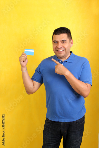 Dark-haired 40-year-old Latino adult man shows his credit card very happy to be able to make purchases and have healthy finances