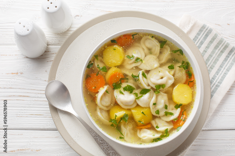 Pelmeni with chicken broth and vegetables closeup on the bowl on the wooden table. Horizontal top view from above