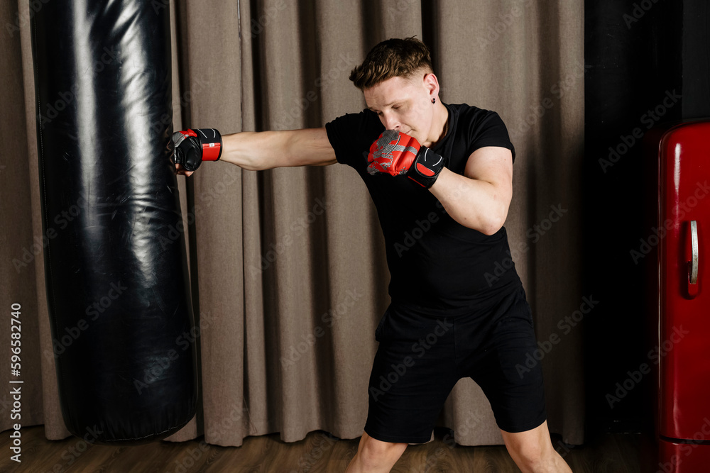 Boxer training with a punching bag in a cozy beige studio, throwing a punch.