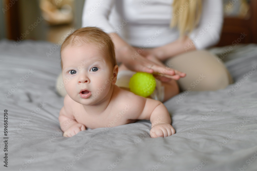 Mom massages the back of the baby with a massage ball. The baby lies on