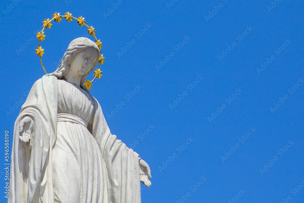 Fototapeta premium Virgin Mary is Queen of heaven. Antique statue against blue sky. Copy space.