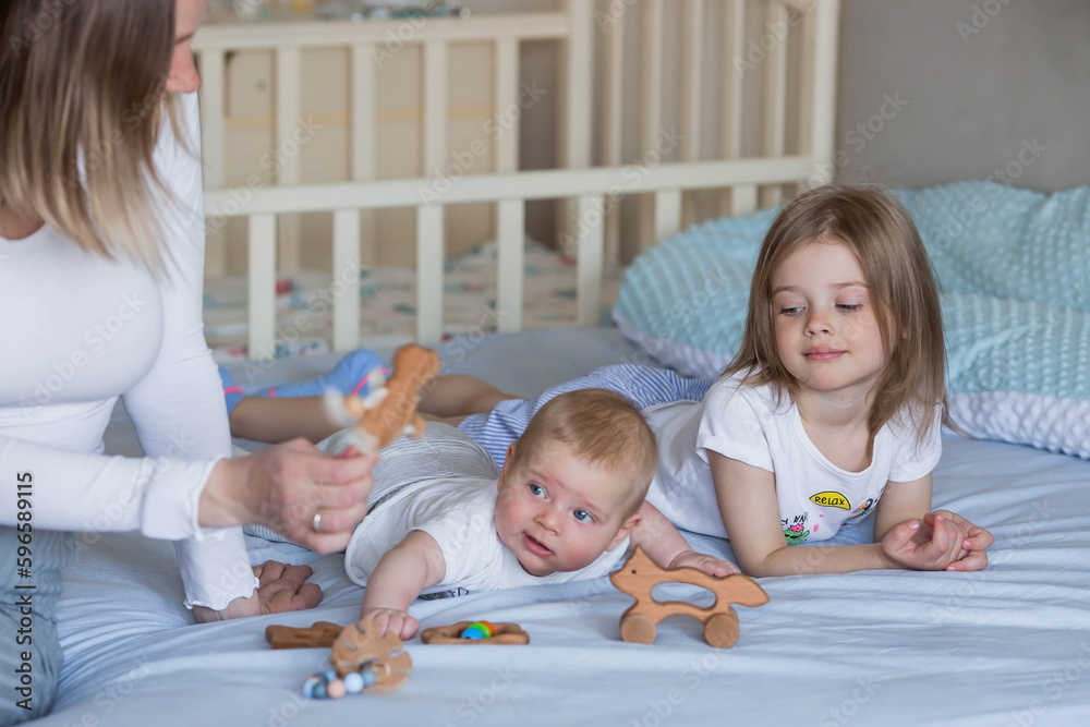 Family, childhood and love. A little girl and a mom in bed in a bright bedroom playing with her younger newborn brother. Children, motherhood. Family, childhood and love. A little girl and a mom in bed in a bright bedroom playing with her younger newborn brother. Children, motherhood.