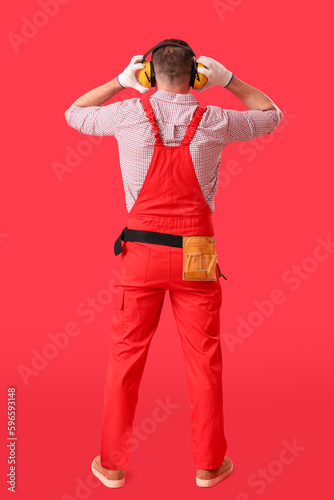 Mature carpenter in hearing protectors on red background, back view