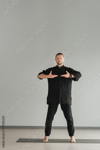 A man in black kimano practicing qigong energy exercises indoors photo