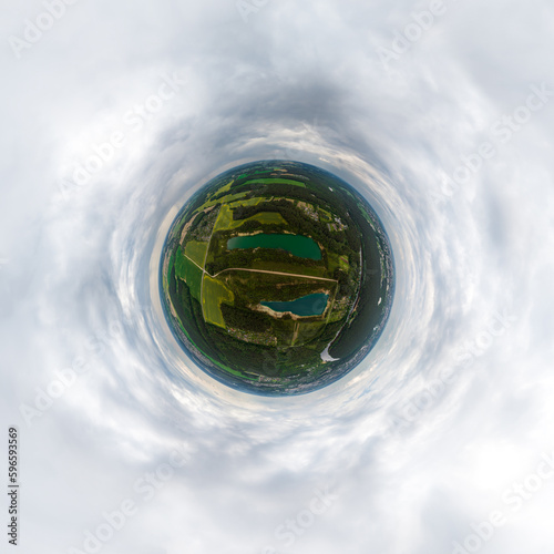 green tiny planet in blue overcast sky with beautiful clouds with transformation of spherical panorama 360 degrees. Spherical abstract aerial view. Curvature of space.