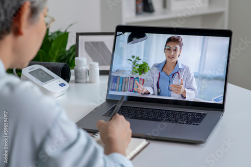 Asian woman with laptop during an online consultation with her doctor in her living room, telemedicine concept