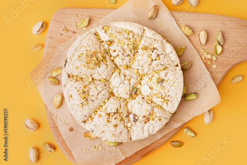 Wooden board of tasty Tahini halva with pistachios on yellow background photo