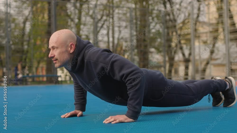 A bald man in a sportswear is exercising on a sports playground. The amateur athlete is doing workout. Sportsman is doing push ups. A bald man in a sportswear is exercising on a sports playground. The amateur athlete is doing workout. Sportsman is doing push ups.