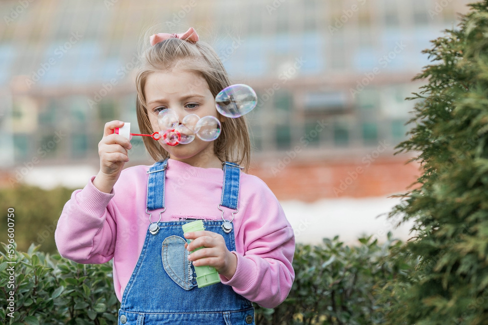 Cute happy girl playing with soap bubbles on a summer day. A child in the fresh air, in nature. The concept of a happy childhood and a holiday. Cute happy girl playing with soap bubbles on a summer day. A child in the fresh air, in nature. The concept of a happy childhood and a holiday.