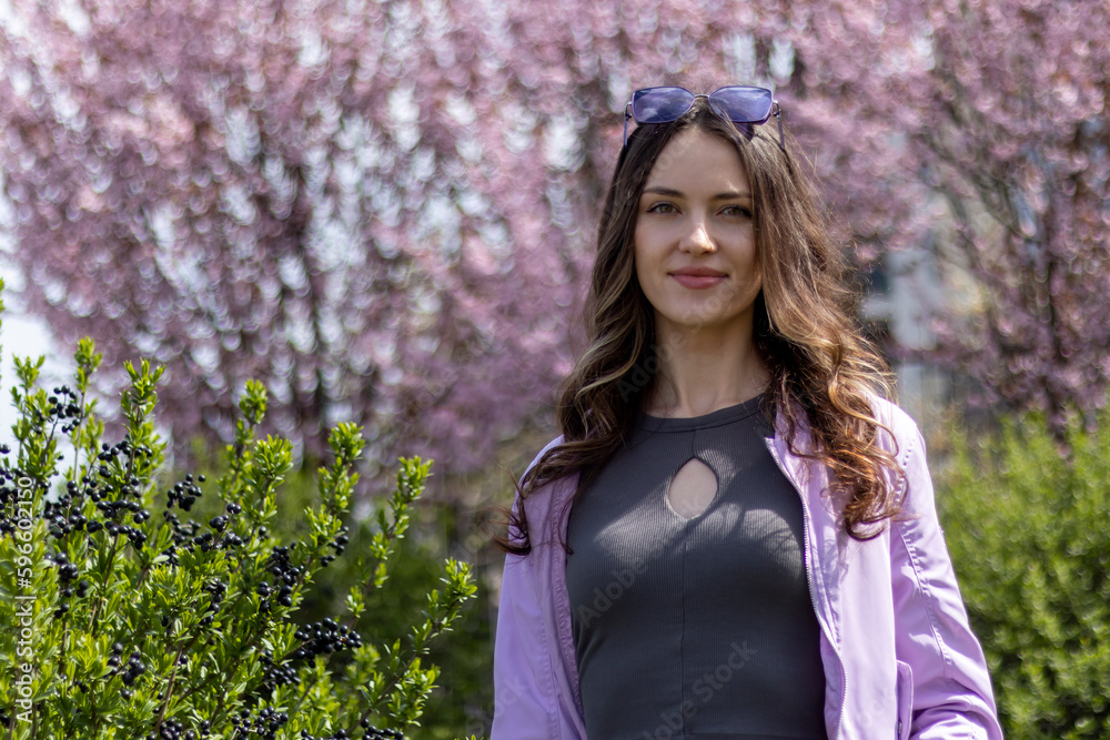 A beautiful happy young woman in fashionable spring purple clothes against a background of a flowering tree and bush. A beautiful happy young woman in fashionable spring purple clothes against a background of a flowering tree and bush.