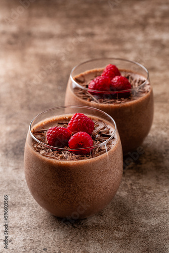 Close-up of homemade chocolate mousse decorated with raspberries and dark chocolate sprinkles in portion glasses. Brown table surface. Vertical image, selective focus.