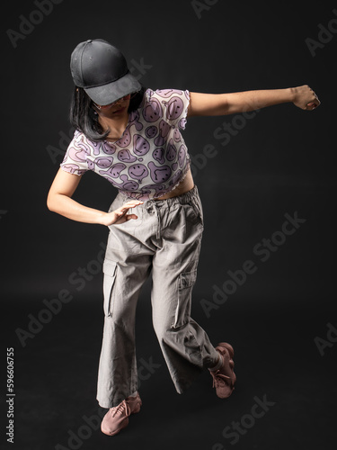 A portrait of a casual fashion style Asian Girl wearing a black cap posing with a Hip hop style. Isolated on Black Background with a red spotlight © Daniel