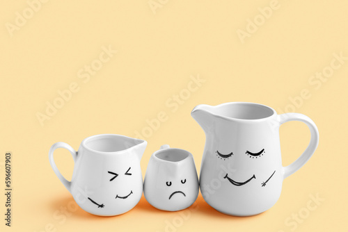 Pitchers with funny faces on beige background. Friendship Day celebration
