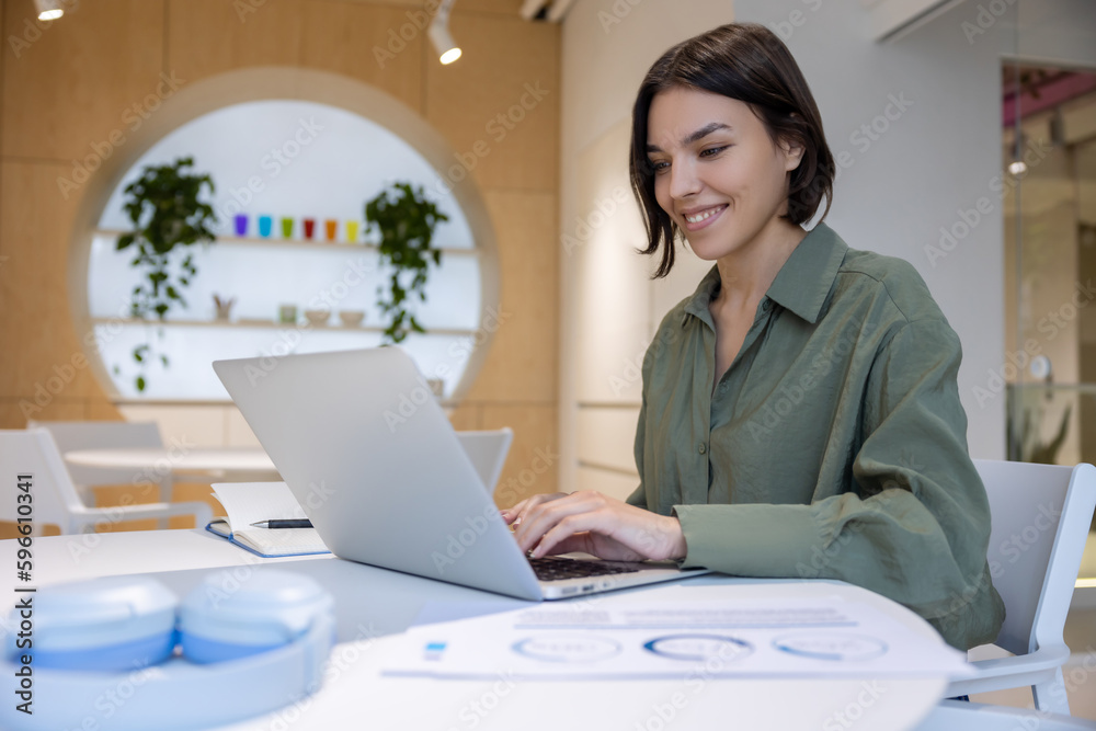 Cheerful office worker typing on the laptop indoors Cheerful office worker typing on the laptop indoors