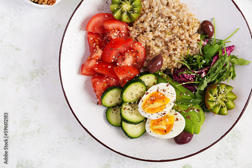 Breakfast oatmeal porridge with boiled eggs, fresh salad and kiwi. Healthy balanced food. Top view, overhead
