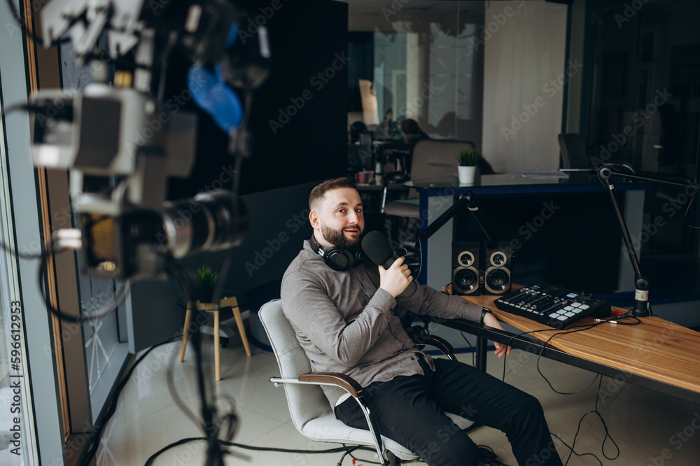Handsome young latin man working as radio host at radio station sitting in front of microphone holding clipboard and using mobile phone. Handsome young latin man working as radio host at radio station sitting in front of microphone holding clipboard and using mobile phone.