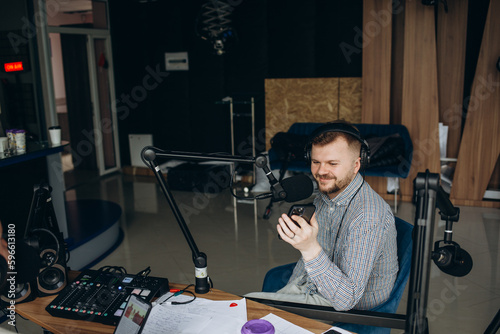 Portrait of young male radio host having a drink, looking focused while speaking in microphone, moderating a live show.