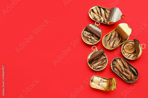 Opened tin cans with different fish on red background