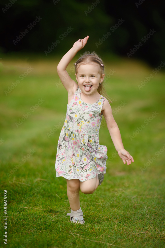 Portrait of a girl in a summer dress running across the field in summer with her tongue hanging out. Interaction of children and nature, fun summer activities, freedom, children's day Portrait of a girl in a summer dress running across the field in summer with her tongue hanging out. Interaction of children and nature, fun summer activities, freedom, children's day