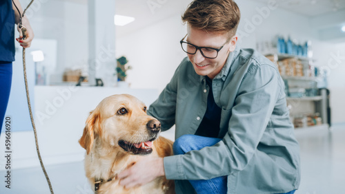 Young Veterinarian Brings a Pet Golden Retriever Back to the Guardian. A Young Man Waiting for His Pet in the Veterinary Clinic Reception Room. Dog is Happy to See the Owner and Get Petted © Gorodenkoff