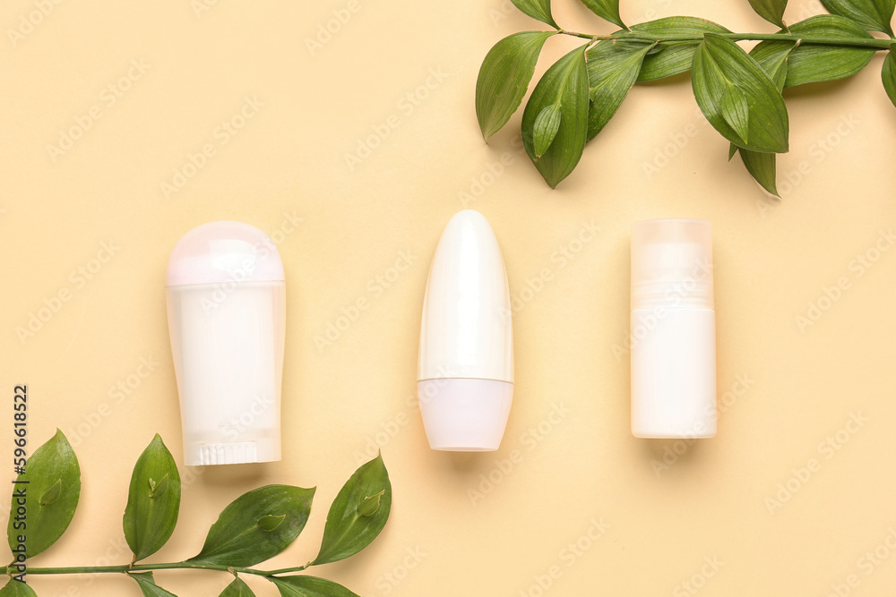 Different deodorant bottles and leaves on yellow background