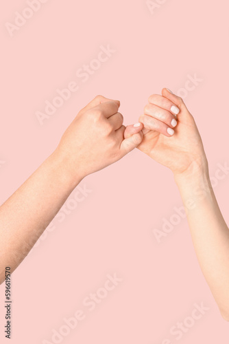 Hands of friends making pinky promise on color background