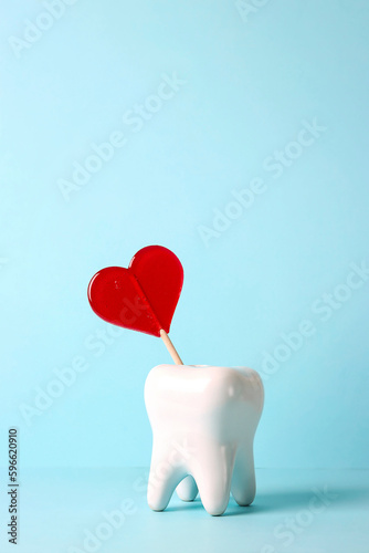 White human tooth with a red heart-shaped lollipop on a blue background.