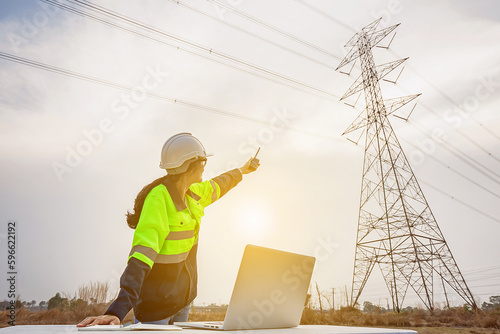 Fotografia Asian female electrical engineer working inspecting power station near high voltage pylons with laptop computer and walkie talkie