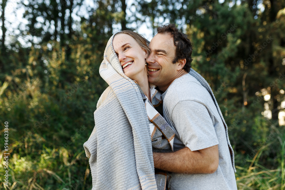 Romantic affectionate couple on a holiday. Man and woman standing together in balcony wrapped in blanket. Couple embracing and smiling Romantic affectionate couple on a holiday. Man and woman standing together in balcony wrapped in blanket. Couple embracing and smiling