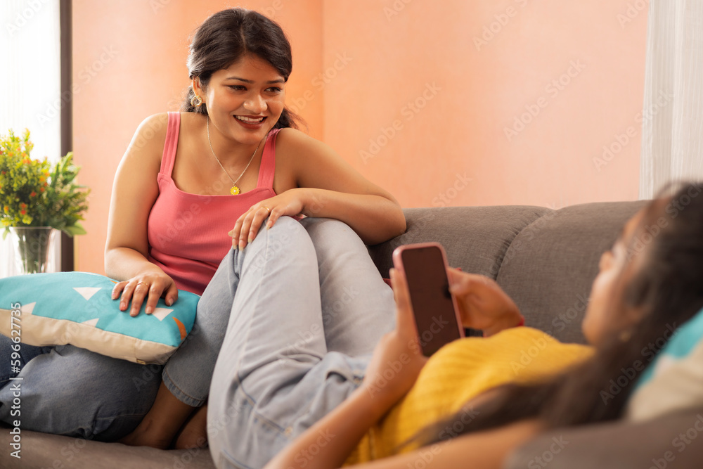Two young women relaxing on sofa in living room