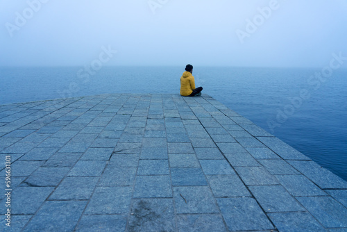 Woman with a yellow jacket looking at the horizon on a pier on a very foggy day at Lake Sanabria. Zamora, Spain. photo
