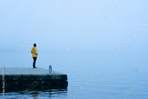 Woman with a yellow jacket looking at the horizon on a pier on a very foggy day at Lake Sanabria. Zamora, Spain. photo