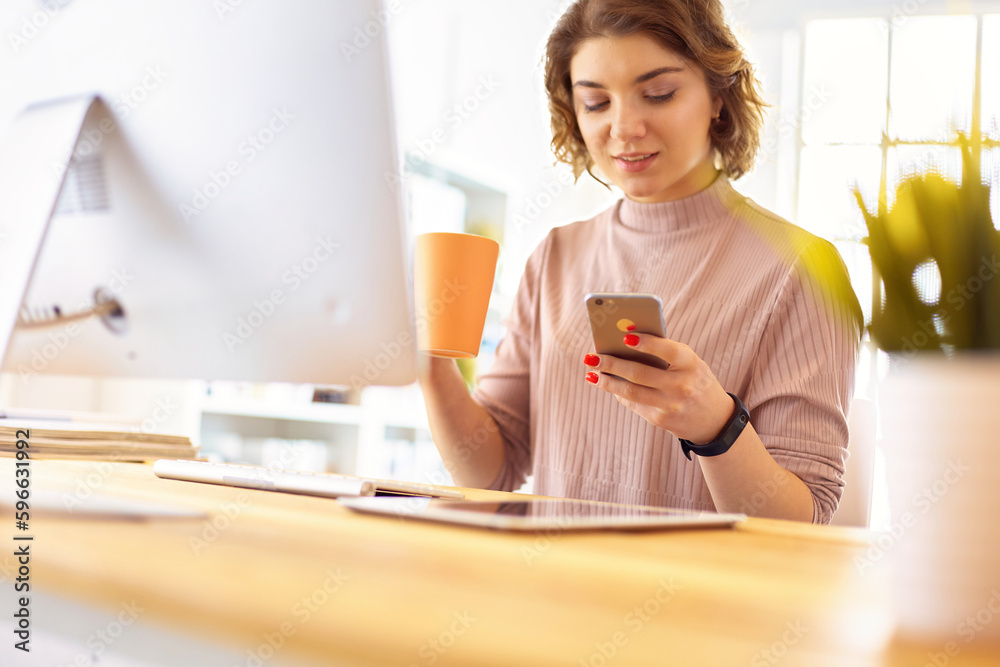 Young businesswoman text messaging while sitting at office in front of laptop. Young businesswoman text messaging while sitting at office in front of laptop.