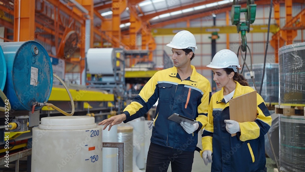 Two industry engineers in hard hats standing at steel metal manufacturing factory checking production process at factory Two industry engineers in hard hats standing at steel metal manufacturing factory checking production process at factory
